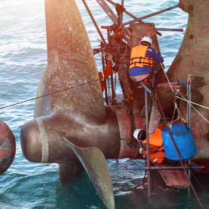 Shipfitter worker wearing a high-visibility vest working on a large cargo ship propeller.
