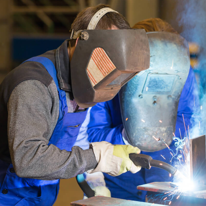 A welding educator monitors a student at work